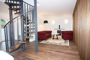 A modern living room with a spiral staircase, red sofas, a round table, and a wooden floor.