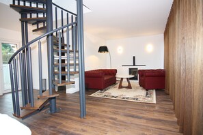Een moderne woonkamer met een spiltrap, rode banken, een ronde tafel en een houten vloer.