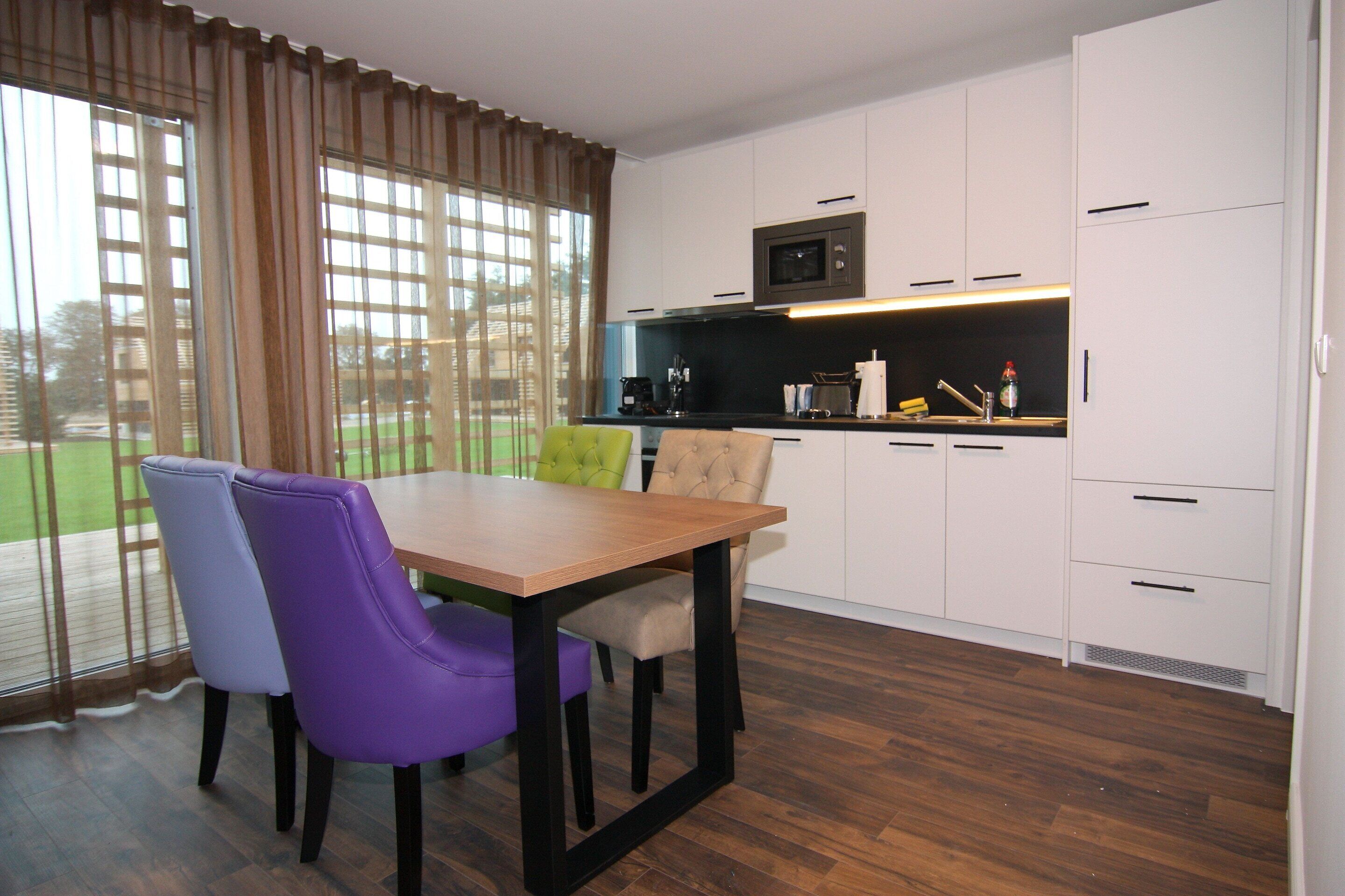 Een moderne keuken met witte kasten, een houten eettafel en paarse stoelen.