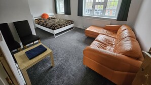 A compact room with a bed, a sofa, a chair, and a small table. - Standard Single Room - Shared (Windsor)