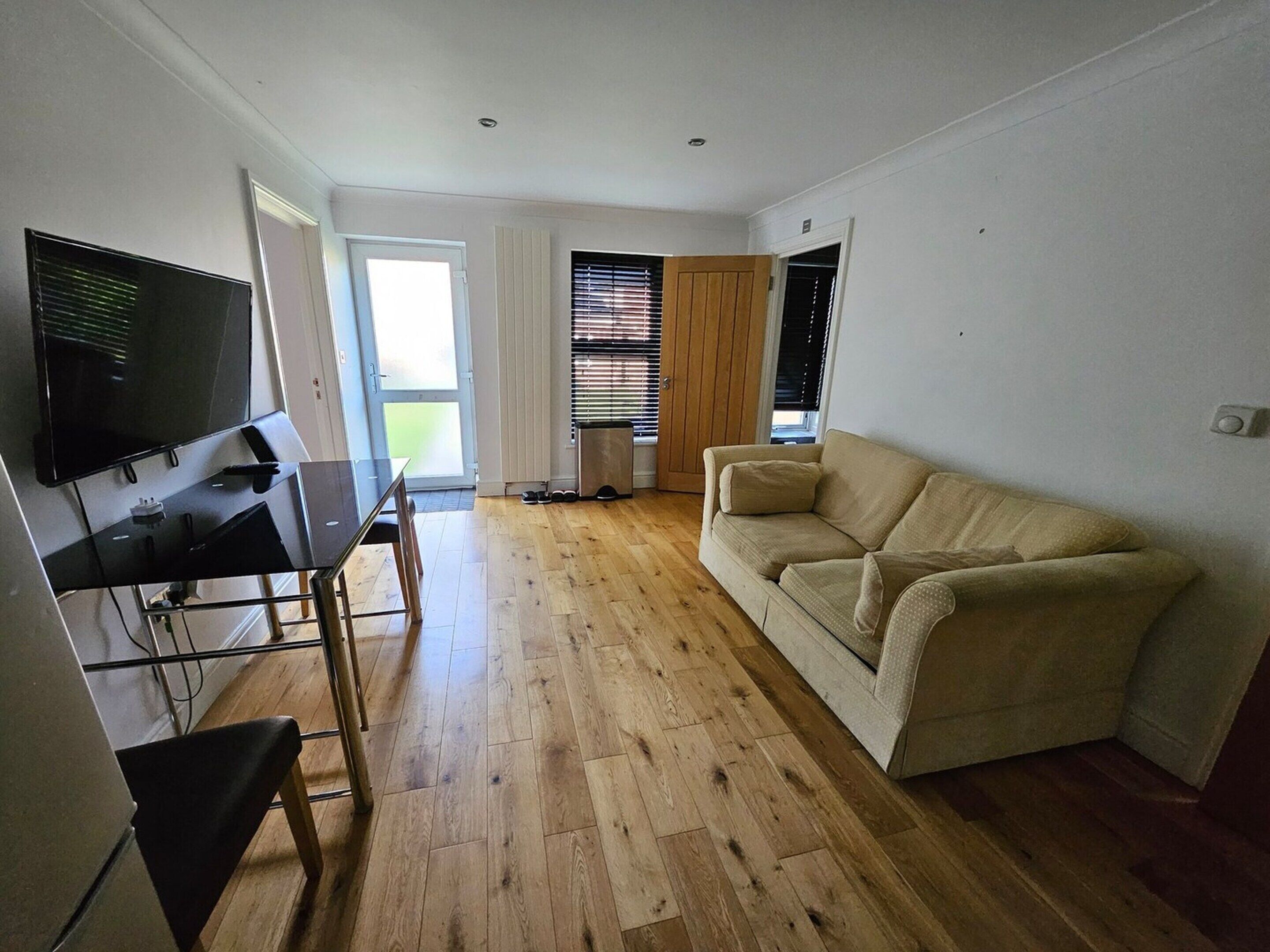 A living room with a beige sofa, a TV mounted on the wall, and a wooden floor.