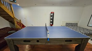 A ping pong table in a room with a wooden floor, a staircase, and a bed with patterned bedding. - Standard Single Room - Shared (Windsor)