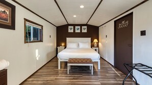 A bedroom with a large bed, a wooden bench, a window, and a door with a towel rack. - Lodge at Deception Pass | Trails, Hot Tub, Walk to Cornet Bay (Oak Harbor)