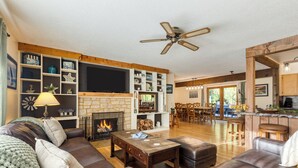 A spacious living room with a fireplace, leather sofas, a coffee table, and a TV mounted on the wall. - Lodge at Deception Pass | Trails, Hot Tub, Walk to Cornet Bay (Oak Harbor)