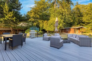 A deck with outdoor furniture, a grill, and a small building in a wooded area. - Lodge at Deception Pass | Trails, Hot Tub, Walk to Cornet Bay (Oak Harbor)