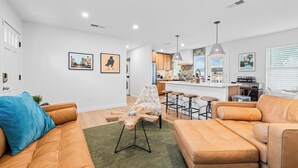 A modern living room with a sofa, a coffee table, and a dining area with bar stools. - Casa Que Canta by AvantStay | Private Pool, Firepit & Walkable East Austin Gem (Austin)