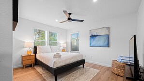 A bedroom with a bed, nightstands, a lamp, a ceiling fan, a painting, and a TV stand. - Casa Que Canta by AvantStay | Private Pool, Firepit & Walkable East Austin Gem (Austin)