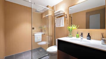 A modern bathroom with a glass shower enclosure, a white toilet, a black sink with a mirror above it, and a vase with flowers on the sink counter.