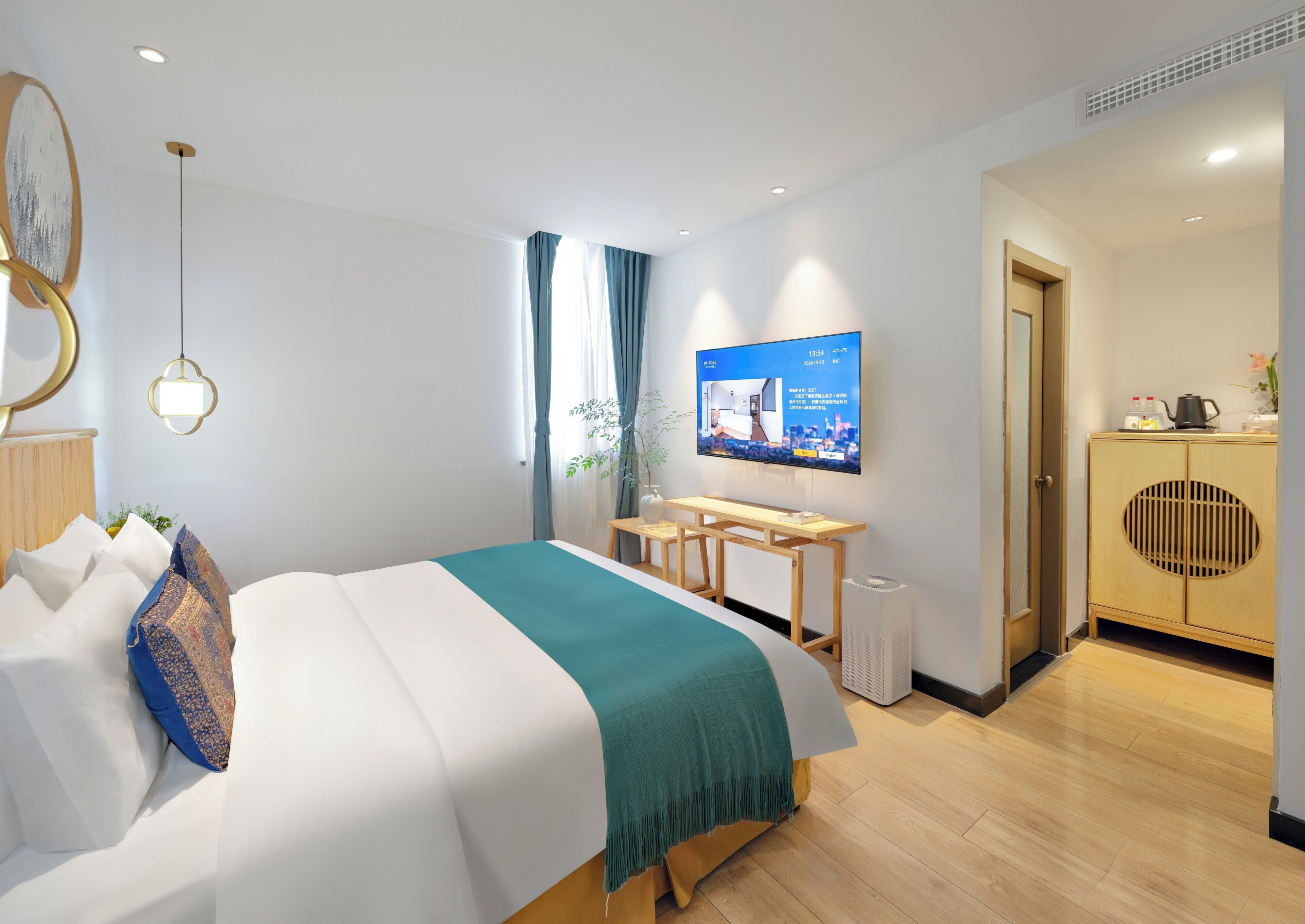A modern hotel room with a bed, a desk, a television, and a wardrobe.