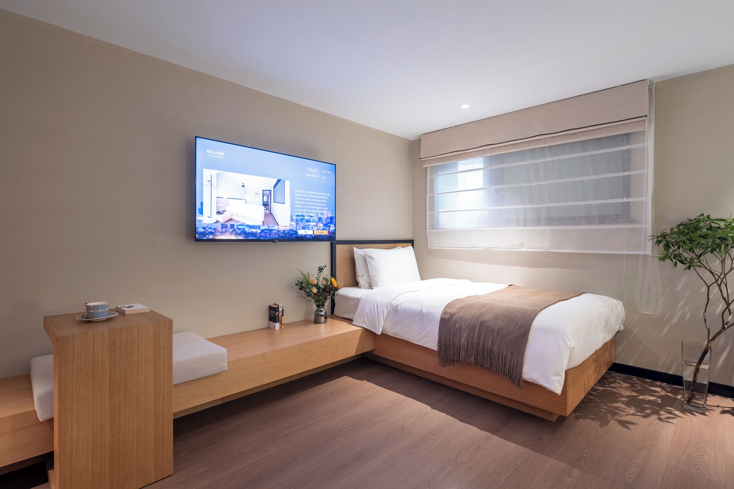 Una habitación de hotel moderna con una cama, una mesita de noche, un televisor montado en la pared y una ventana con persianas.