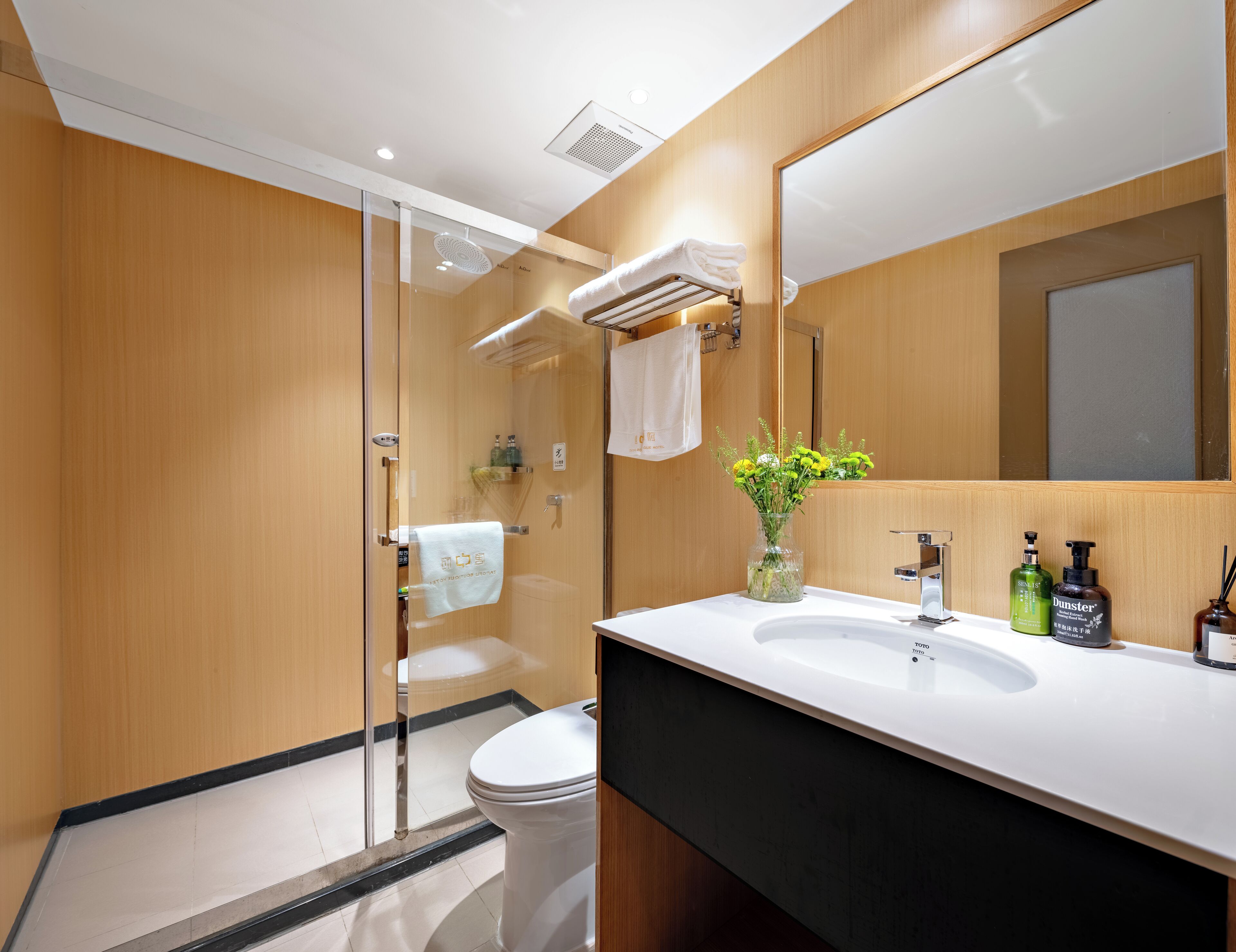 Un baño moderno con cabina de ducha de vidrio, inodoro blanco, tocador con encimera negra y espejo sobre el lavabo.