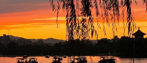 A sunset view with boats on a calm water body, surrounded by a cityscape.