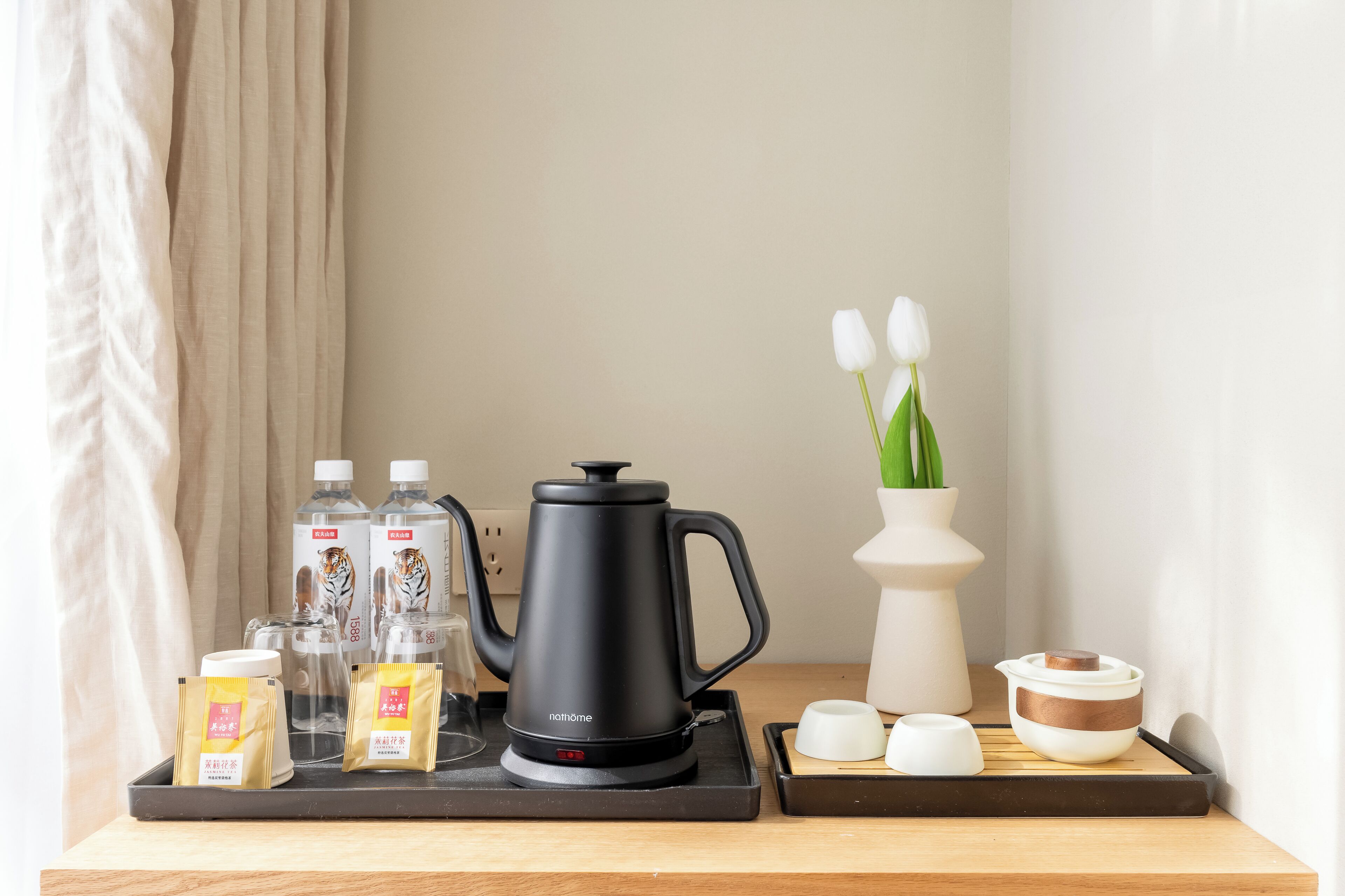 A tray with a black electric kettle, two bottles of water, two glass jars, and a white vase with tulips.