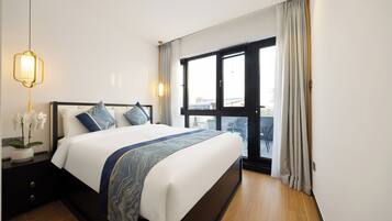 A hotel room with a large bed, a nightstand with a lamp, a window with curtains, and a view of the outside.