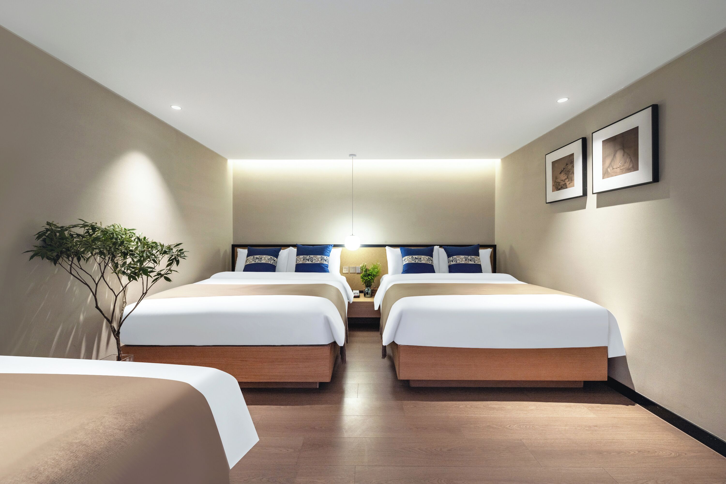 Habitación de hotel con dos camas, una planta y cuadros en la pared.