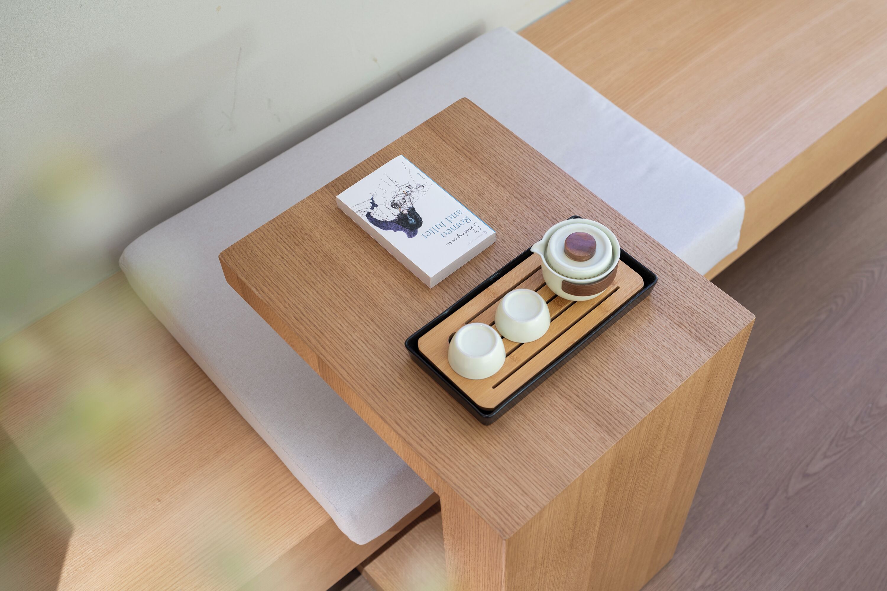 A wooden table with a white cushion, a tray with three white cups, and a card with a black and white illustration.