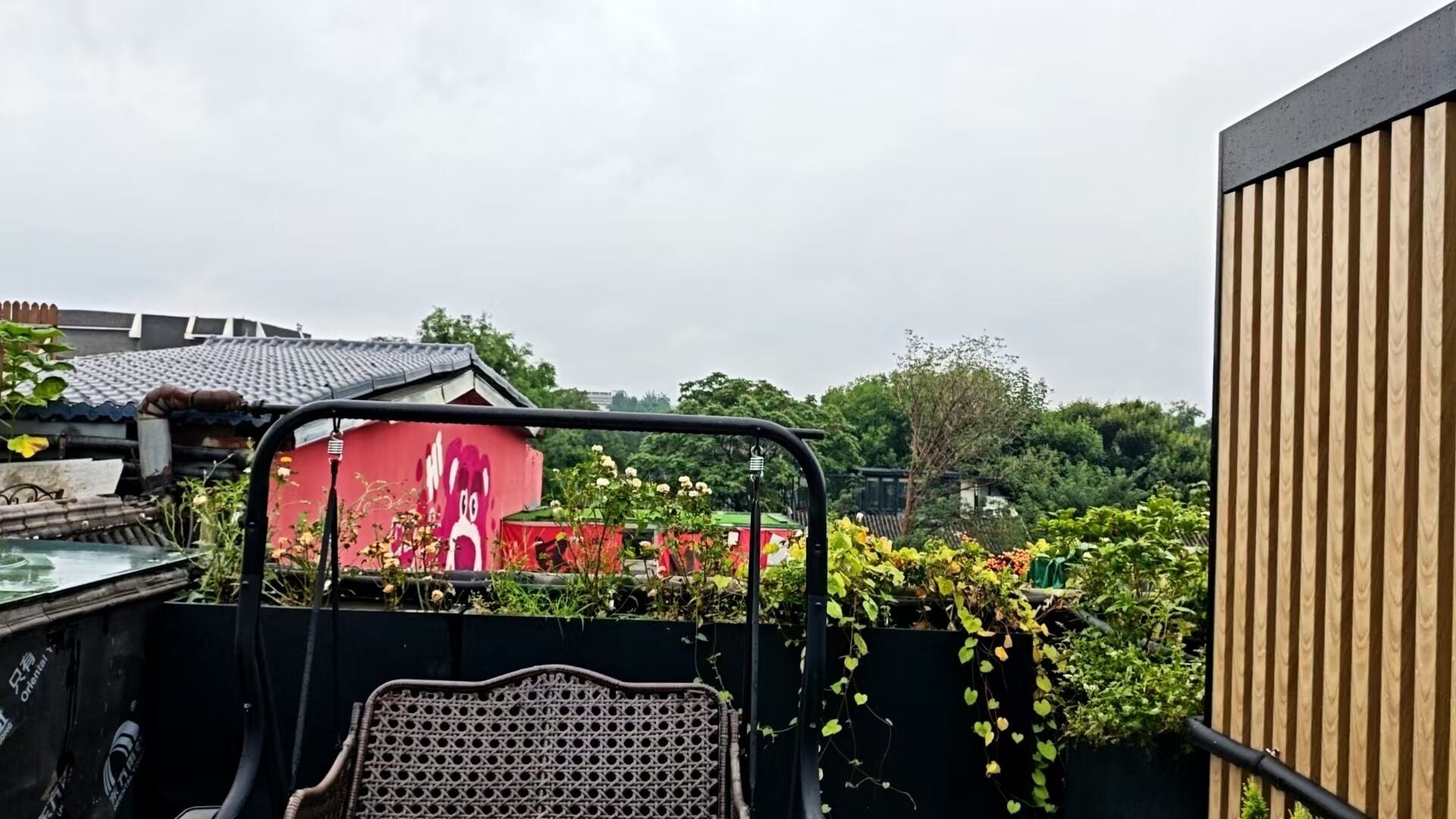 A rooftop garden with a metal chair, a red building with a cartoon character, and a wooden fence.