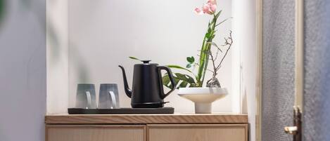 A wooden cabinet with a circular cutout, a black teapot, two glasses, and a potted plant with pink flowers.