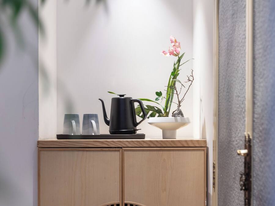 A wooden cabinet with a circular cutout, a black teapot, two glasses, and a potted plant with pink flowers.