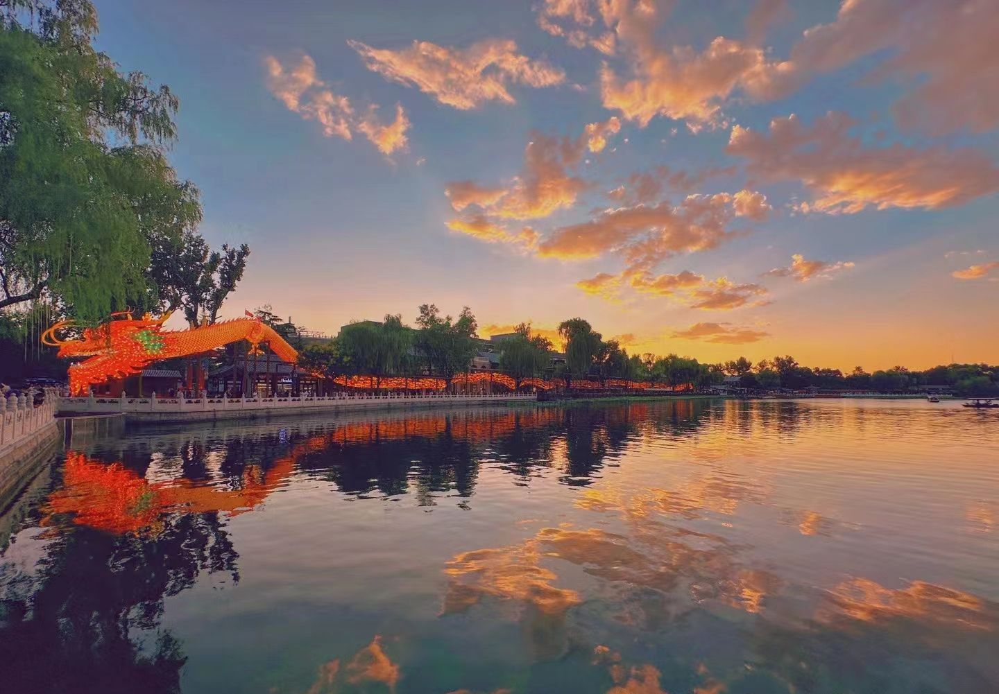 Un coucher de soleil paisible sur un lac, avec un pavillon chinois traditionnel et des décorations en forme de dragon.