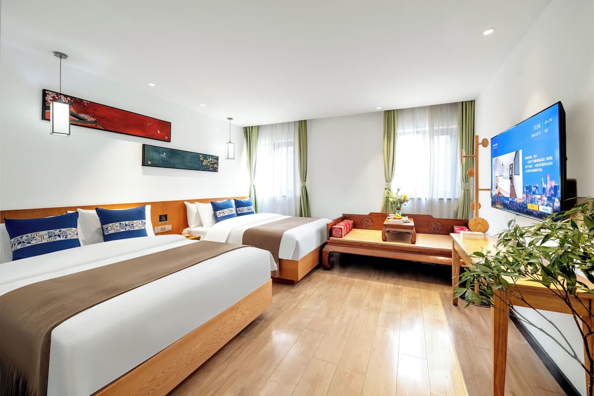 Una habitación de hotel con dos camas, un sofá, un televisor y una planta.