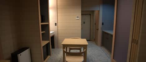 A room with a wooden table and chair, a small white cabinet, and a door in the background.