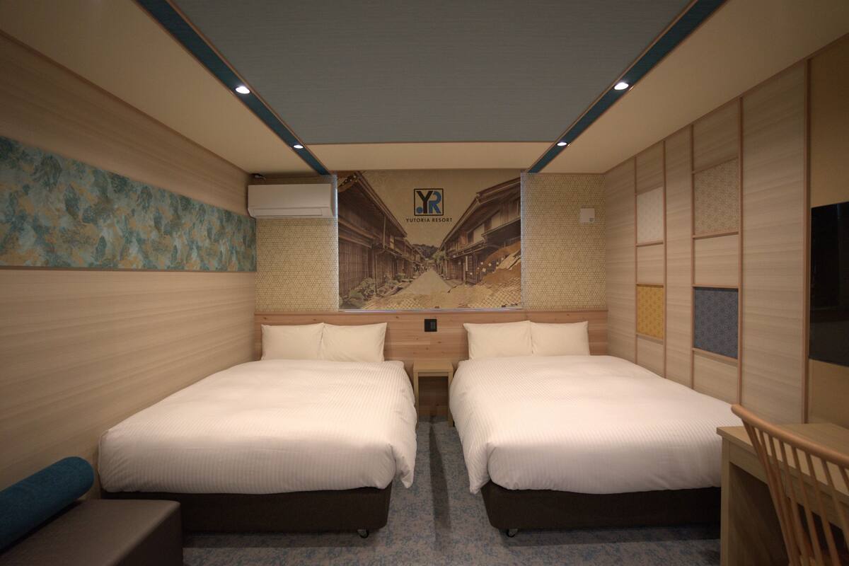 A hotel room with two beds, a small desk, and a wall-mounted TV.