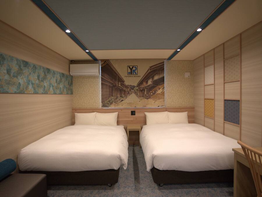 A hotel room with two beds, a small desk, and a wall-mounted TV.