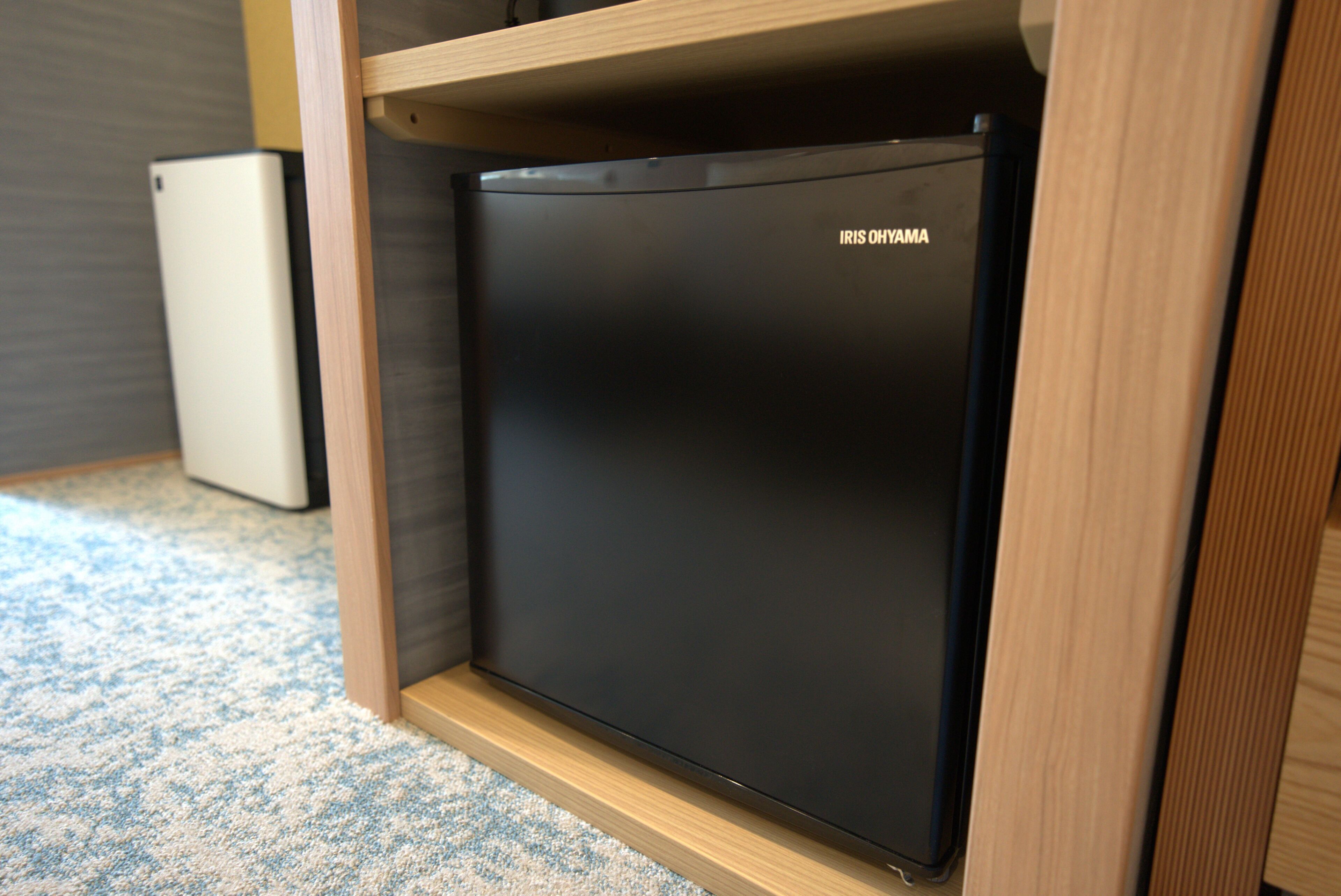 A compact black refrigerator with the brand 'IRIS OHYAMA' in a wooden cabinet.