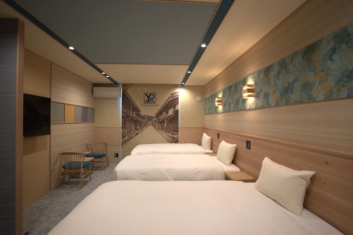 A hotel room with two beds, a television, a chair, and a mural on the wall.