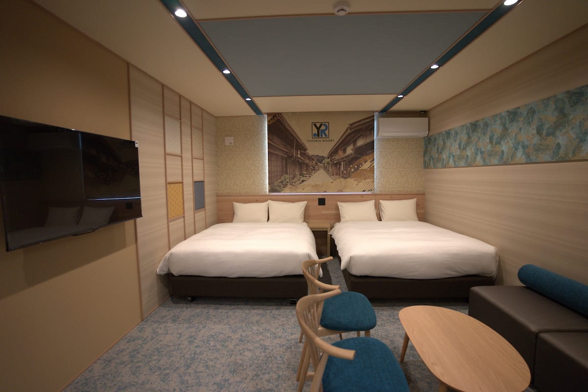 A hotel room with two beds, a TV, a small table, and a chair.