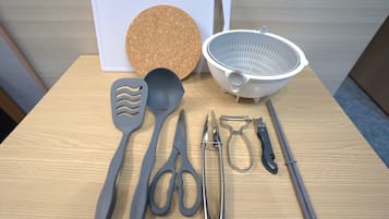 A table with kitchen utensils including a cork mat, colander, spatula, scissors, and tongs.