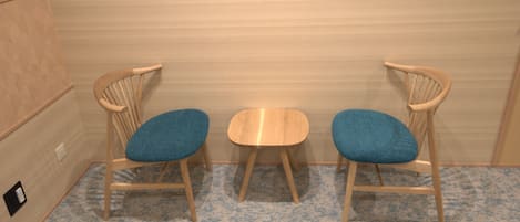 A room with two wooden chairs and a small table, a patterned carpet, and a light-colored wall.