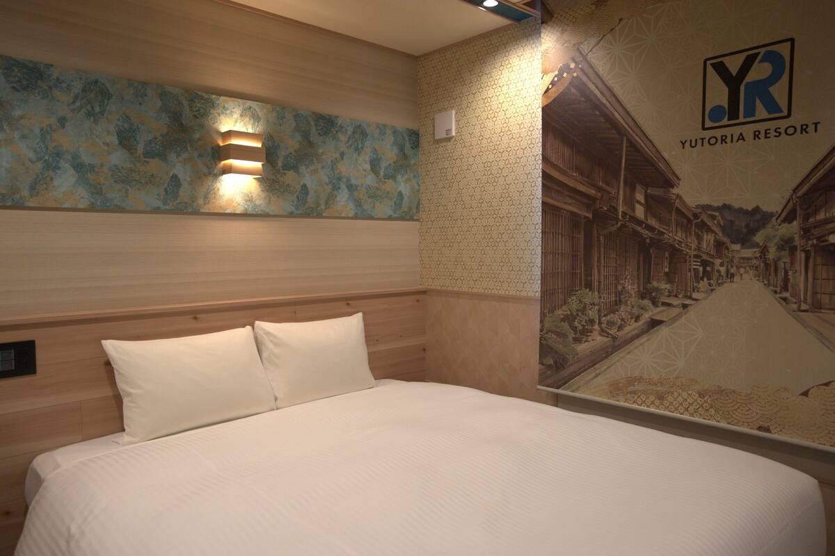A hotel room with a bed, a wall-mounted light, and a mural of a building.