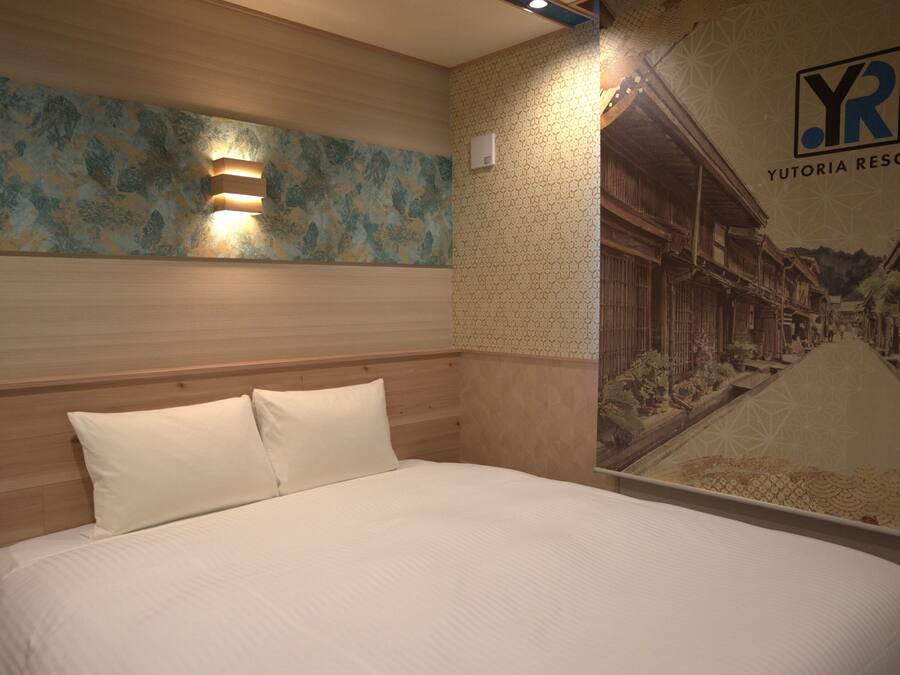 A hotel room with a bed, a wall-mounted light, and a mural of a building.