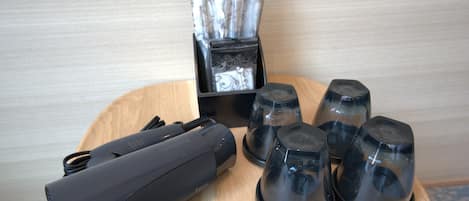 Uma mesa com um aparelho preto, um conjunto de xícaras pretas e uma caixa de lenços.