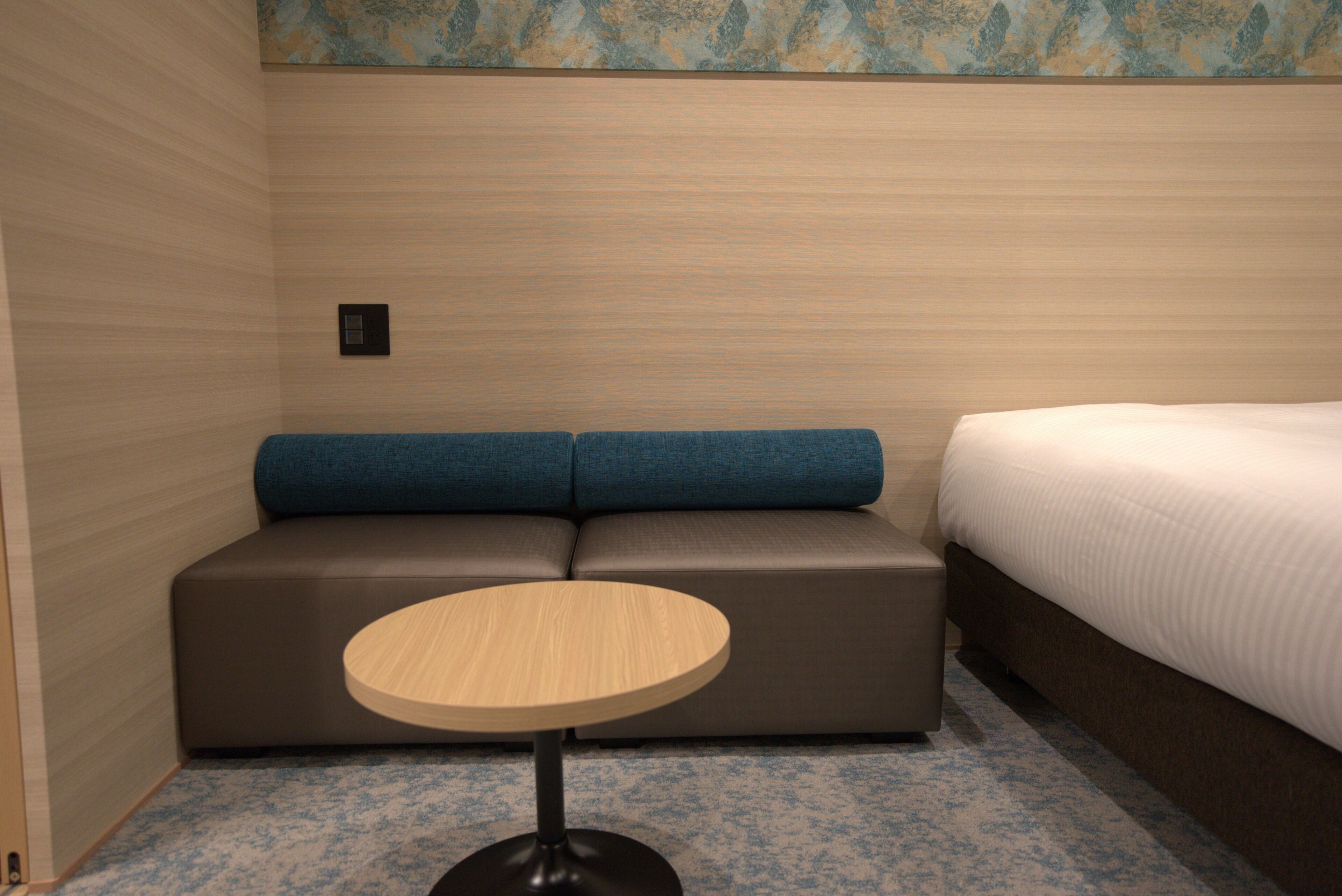 Una habitación con una cama, una pequeña mesa redonda y una zona de estar con cojines.
