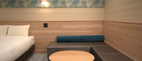 A room with a bed, a small table, a sofa, and a wall-mounted light fixture.