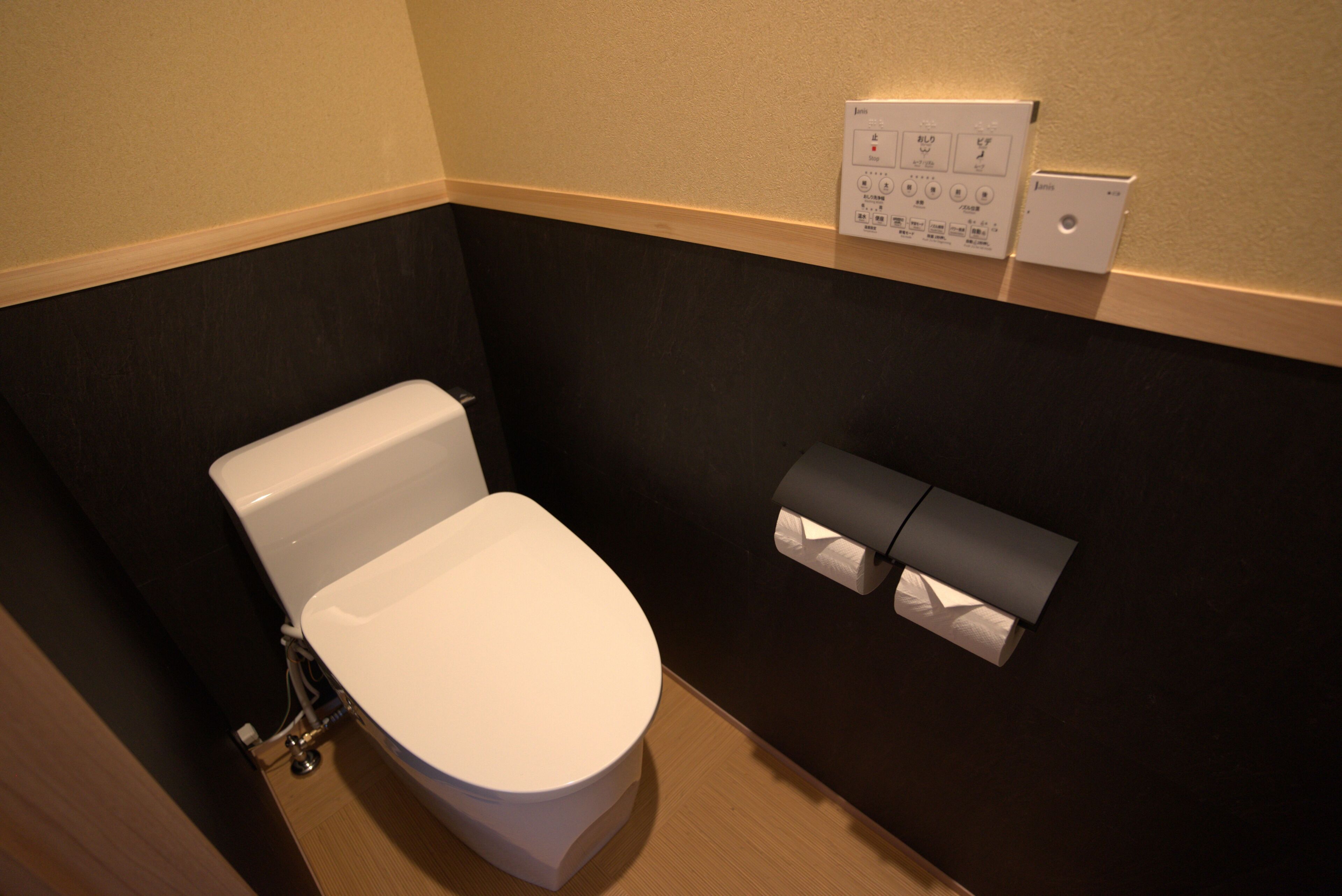 A modern bathroom with a white toilet, a towel dispenser, and a wall-mounted paper towel dispenser.