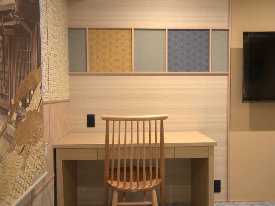 A wooden chair in front of a desk with a patterned wall behind it.