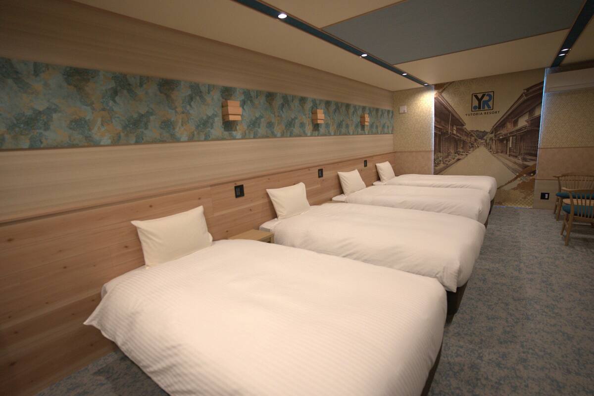A hotel room with four beds aligned against a wall, a wooden headboard, and a mural depicting a street scene.