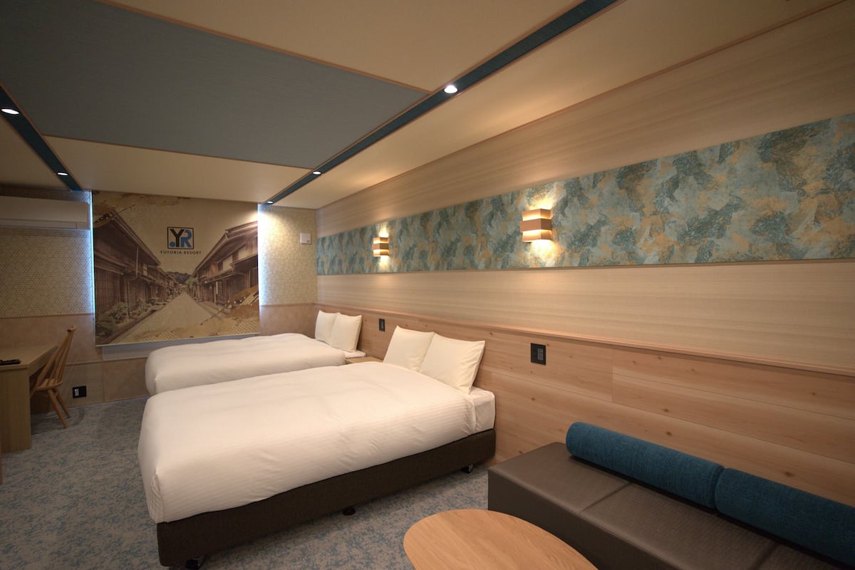 A hotel room with two beds, a desk, a chair, a small table, and a sofa.