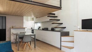 Een moderne keuken met witte kasten, een eethoek met een grijze tafel en stoelen, en een aan de muur bevestigde televisie.