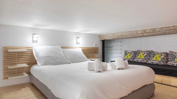 Een moderne slaapkamer met een groot bed, een houten hoofdbord en een ingebouwde bank met kussens.