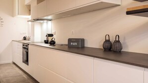 Een moderne keuken met witte kastjes, een roestvrijstalen afzuigkap en een zwarte doos met de tekst 'PAIN' op het aanrecht.