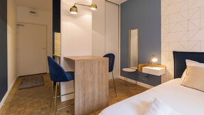 A modern hotel room with a bed, a desk, a chair, a small table, a mirror, and a wall-mounted light fixture. - DIFY Charme - Bord du Rhône (Lyon)