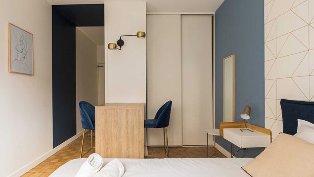 A modern hotel room with a bed, a desk, a chair, a small table with a lamp, and a wardrobe. - DIFY Charme - Bord du Rhône (Lyon)