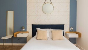 A neatly arranged bedroom with a large bed, two bedside tables, a round mirror, and a geometric-patterned wall. - DIFY Charme - Bord du Rhône (Lyon)