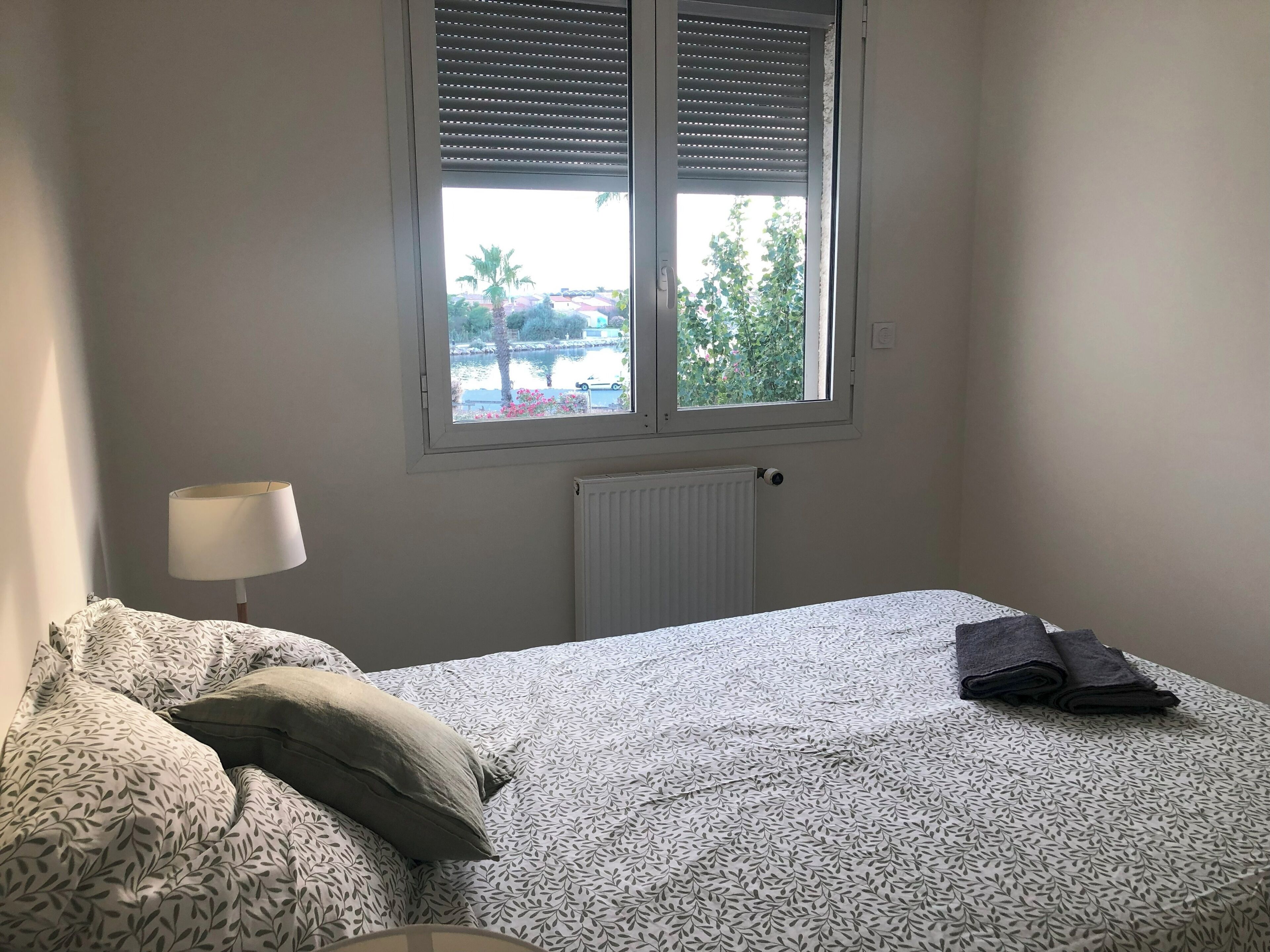 A bedroom with a bed, a window with blinds, a radiator, and a lamp.