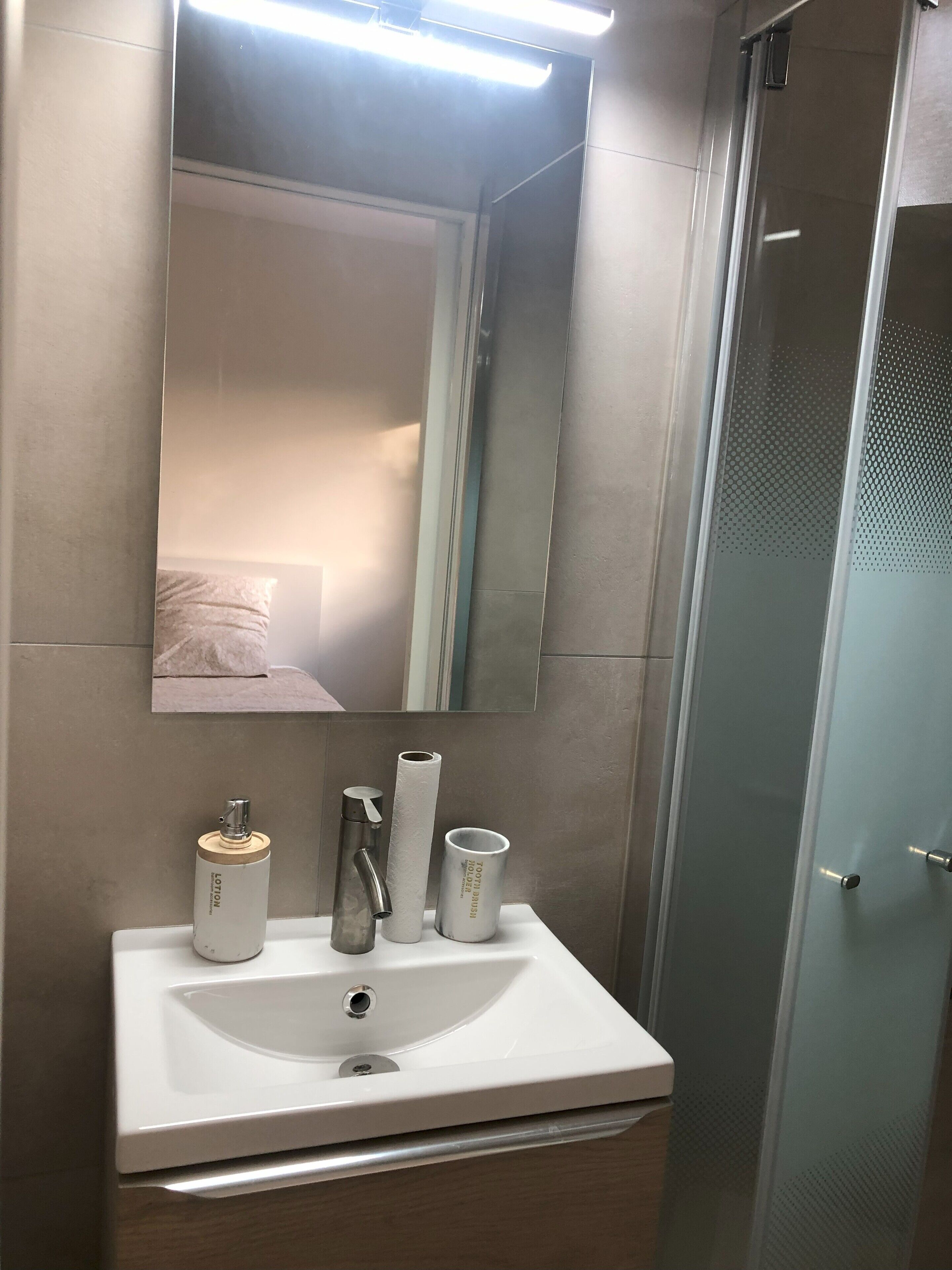 Un baño con un lavamanos blanco, un espejo y una ducha.